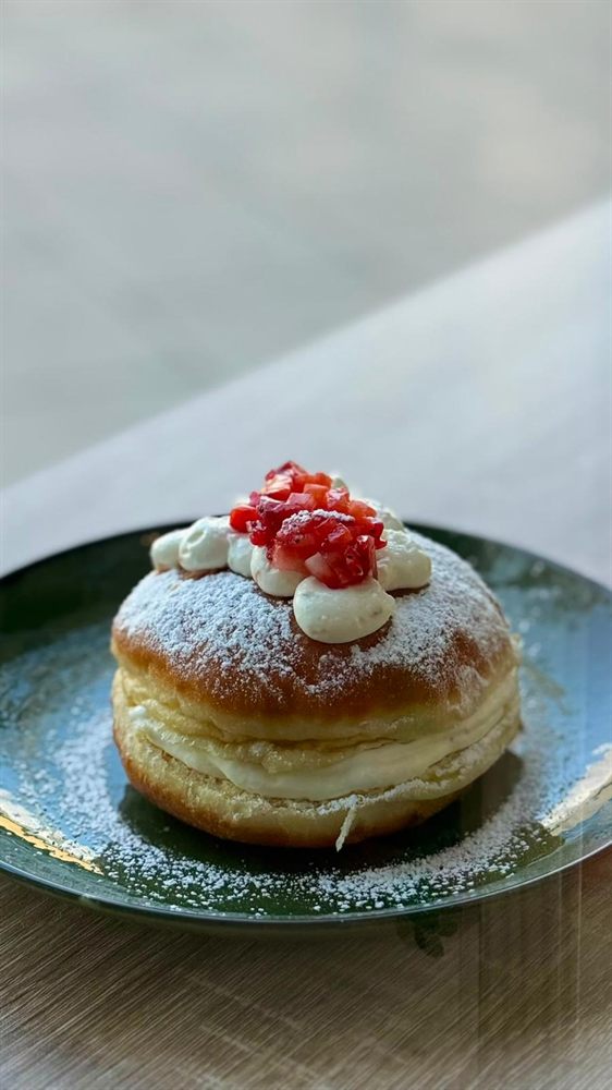 Berlina rellena de nata con frutos rojos en un plato verde.