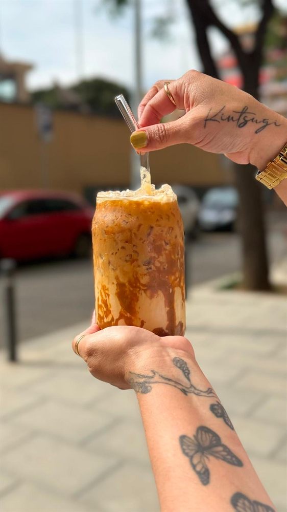 Una mano sostiene un café con hielo para llevar, en la calle.