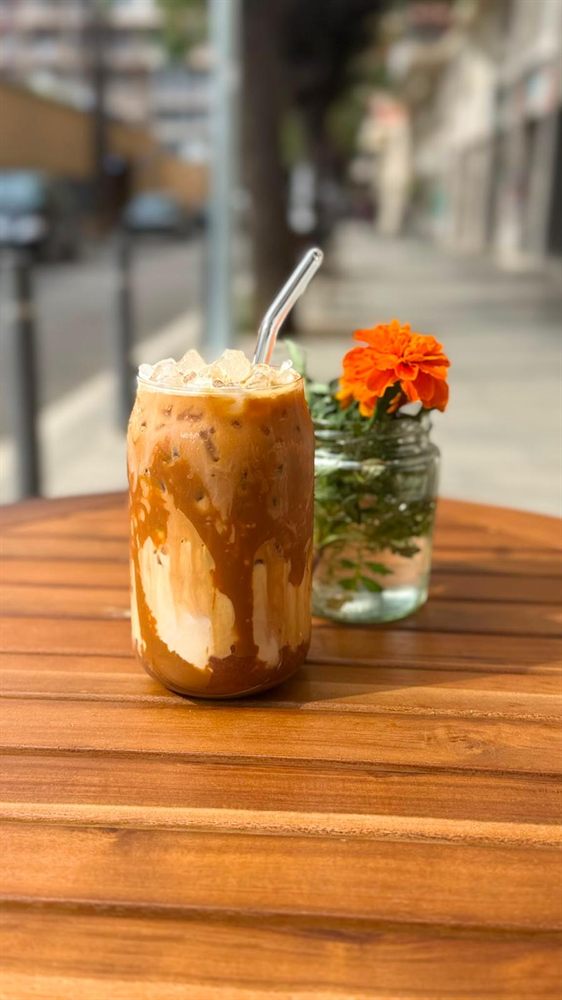 Iced latte con pajita y flores en una mesa de la terraza.