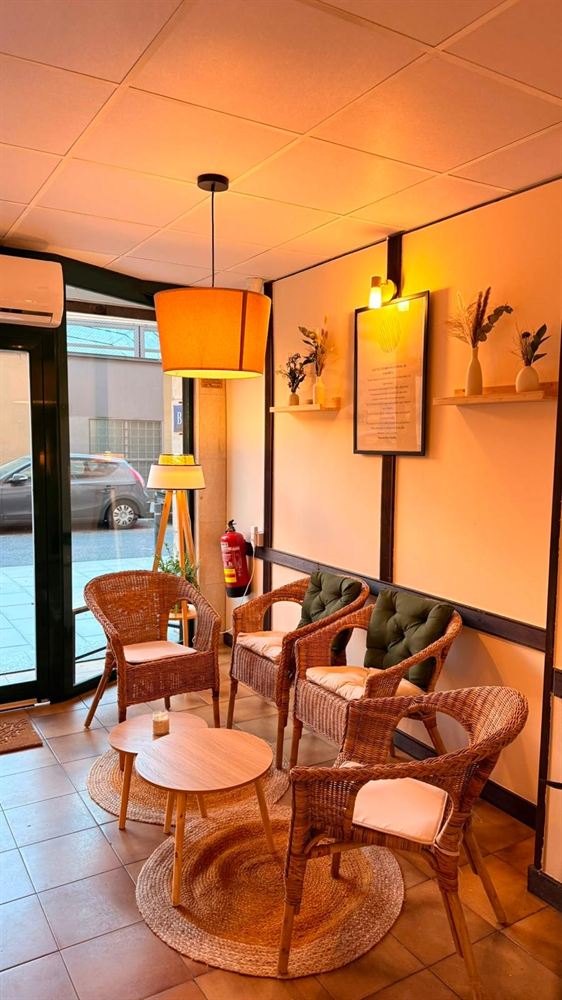 Interior de Lúcido al atardecer: sillas de ratán, lámparas encendidas y luz cálida.