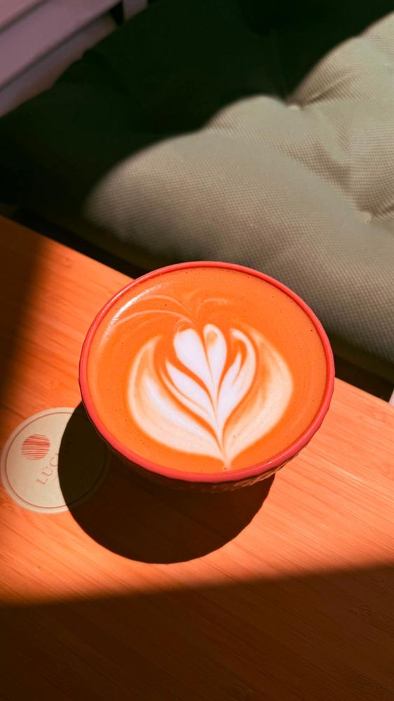 Café con leche con arte latte en taza naranja sobre una mesa de terracota, al sol.