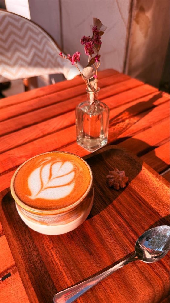 Café con leche con arte latte en la terraza, con una flor en la mesa.