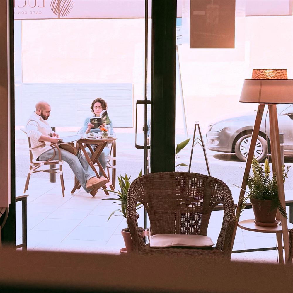 Dos personas charlando en una mesa de Lúcido, vistas desde la calle a través del cristal.