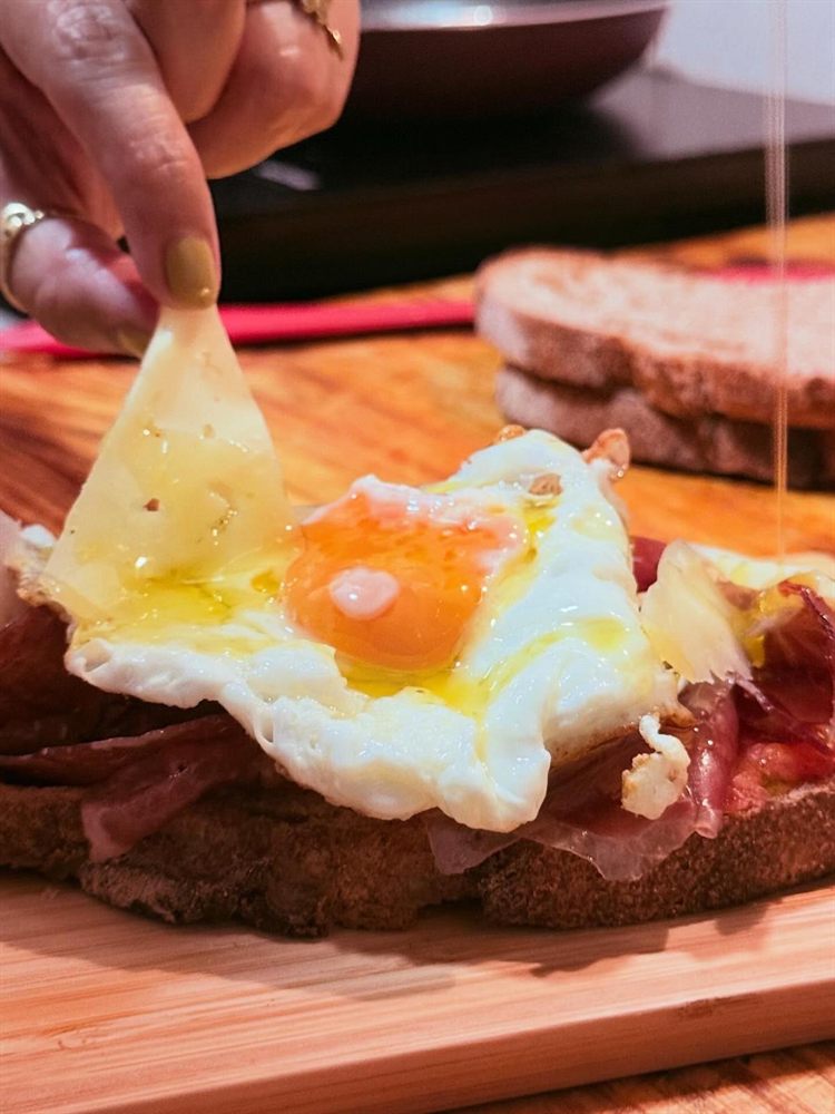 Tostada con queso fundido, huevo y jamón, con una mano estirando el queso.