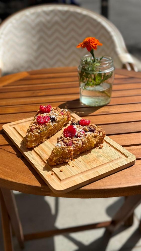 Dos tostadas con fruta y semillas sobre una tabla de madera, en una mesa de la terraza.