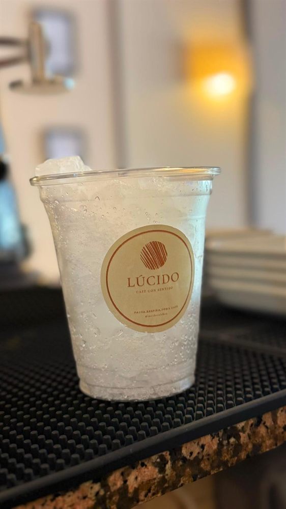Vaso para llevar con el sello de Lúcido, sobre la barra.
